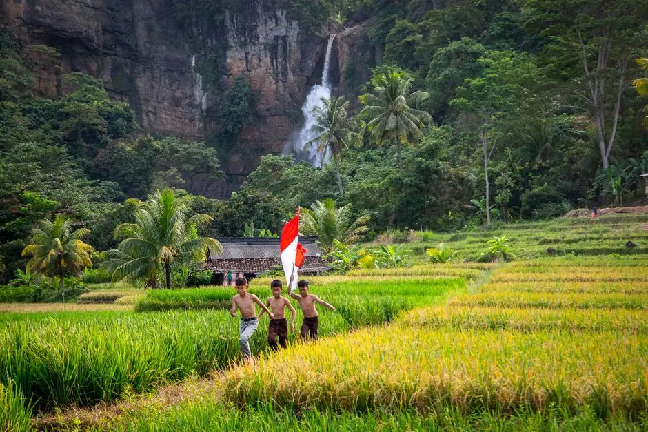 Dua anak bermain di kolam air terjun yang dangkal dengan latar pepohonan hijau